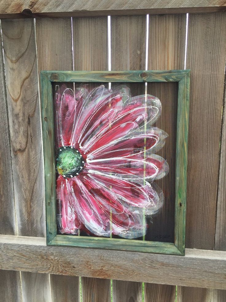 a painted flower in a wooden frame on a fence