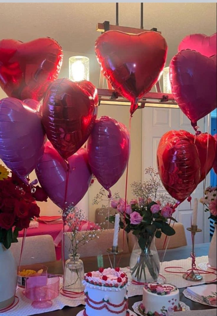 there are many heart shaped balloons in the air over cakes and cupcakes on the table