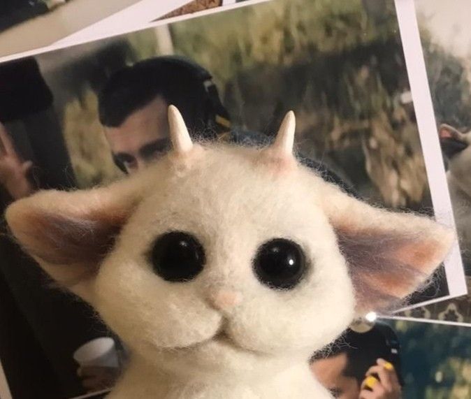 a white stuffed animal with black eyes and horns on it's head next to photos