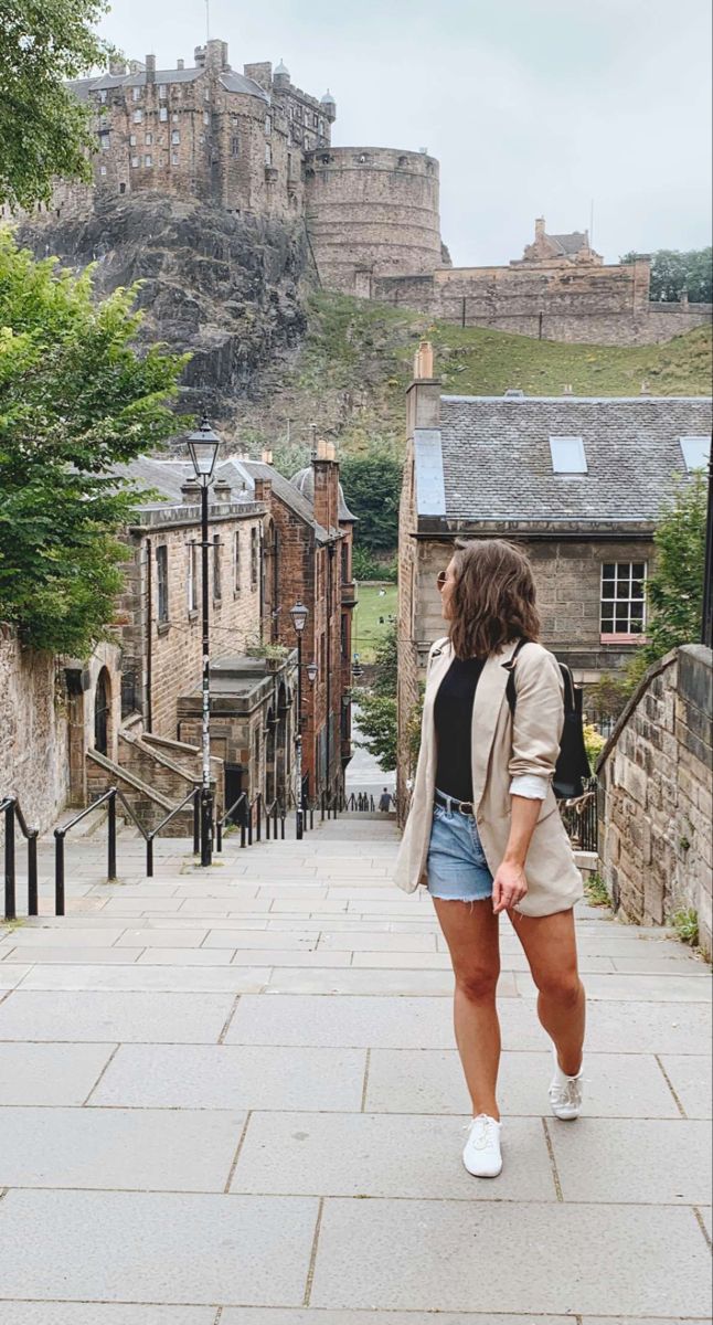 a woman is walking down the street in front of an old castle on a hill