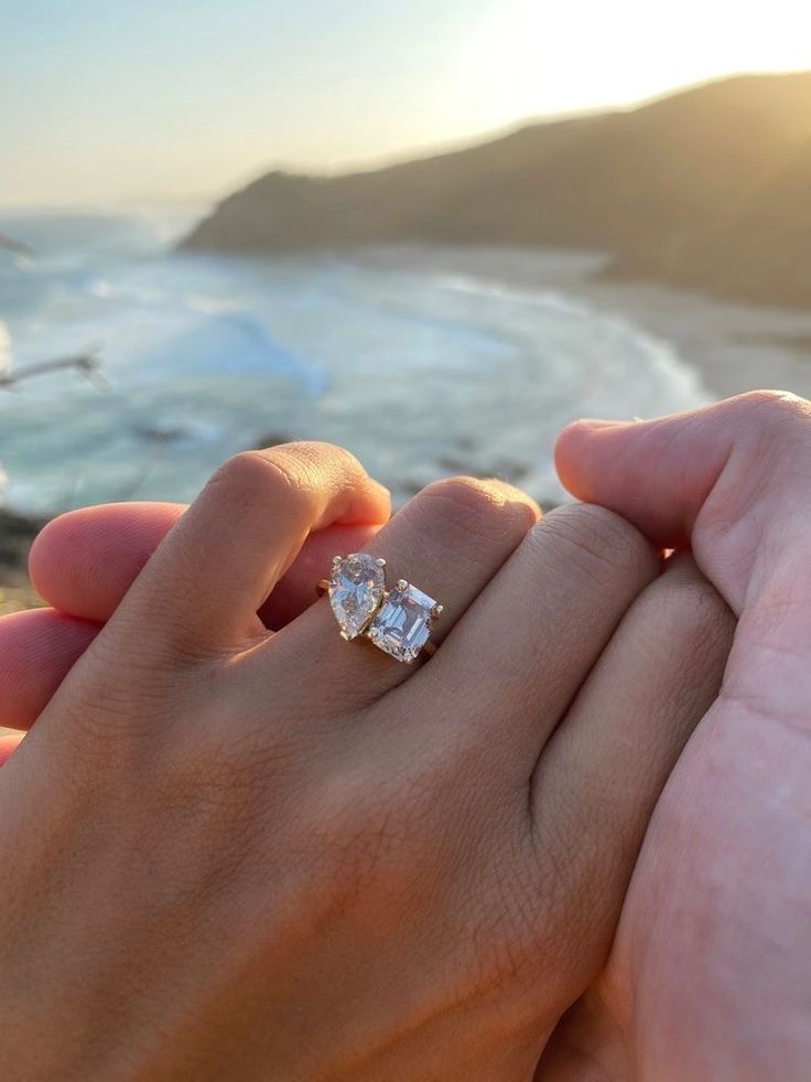 two people holding each other's hands with the ocean in the background