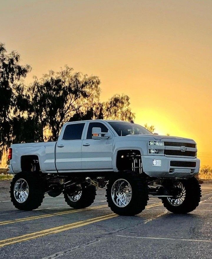 a silver truck parked in a parking lot with the sun setting behind it and trees