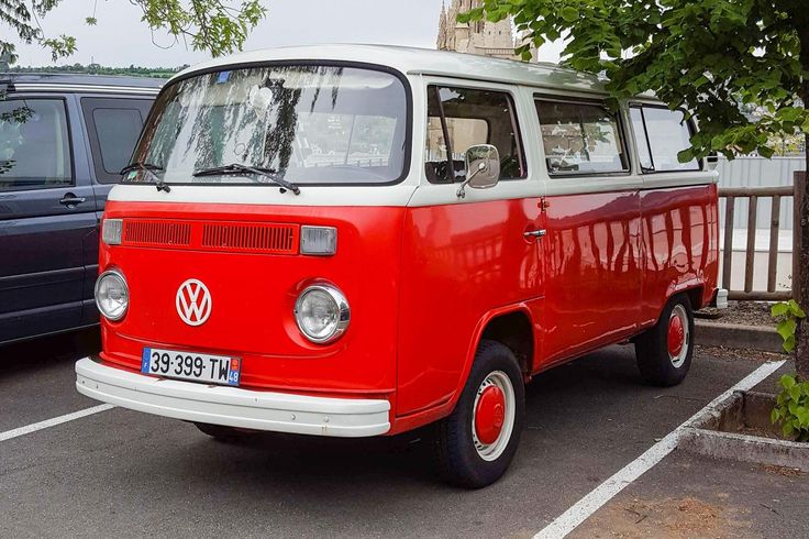 an old red and white van parked in a parking lot next to another blue van