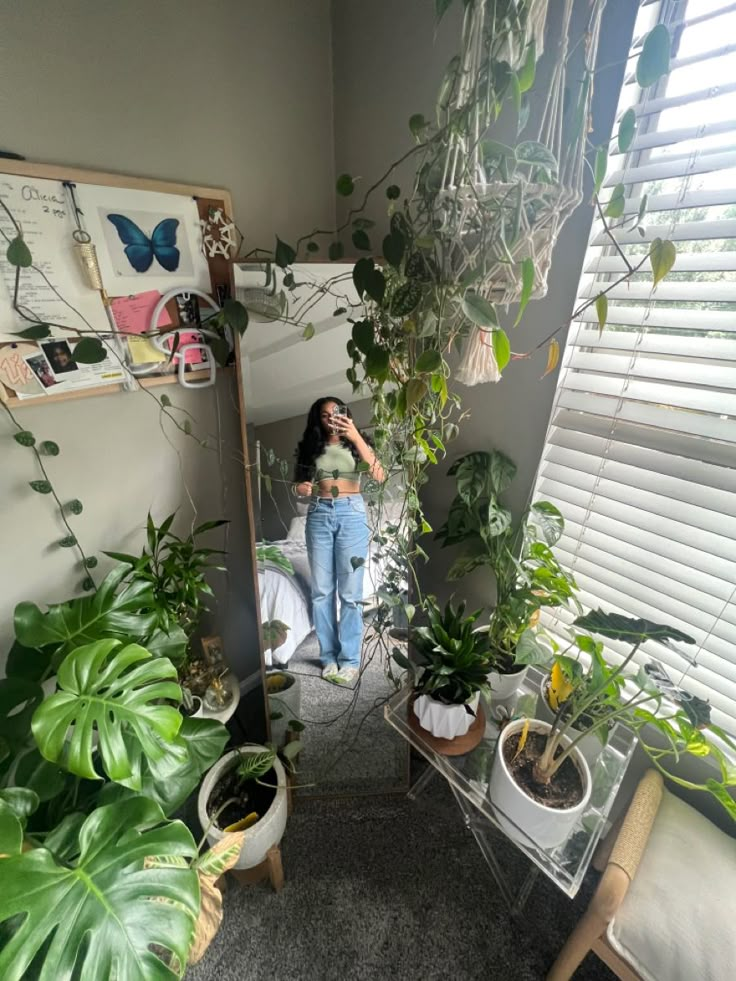 a woman taking a selfie in the mirror next to some houseplants and plants