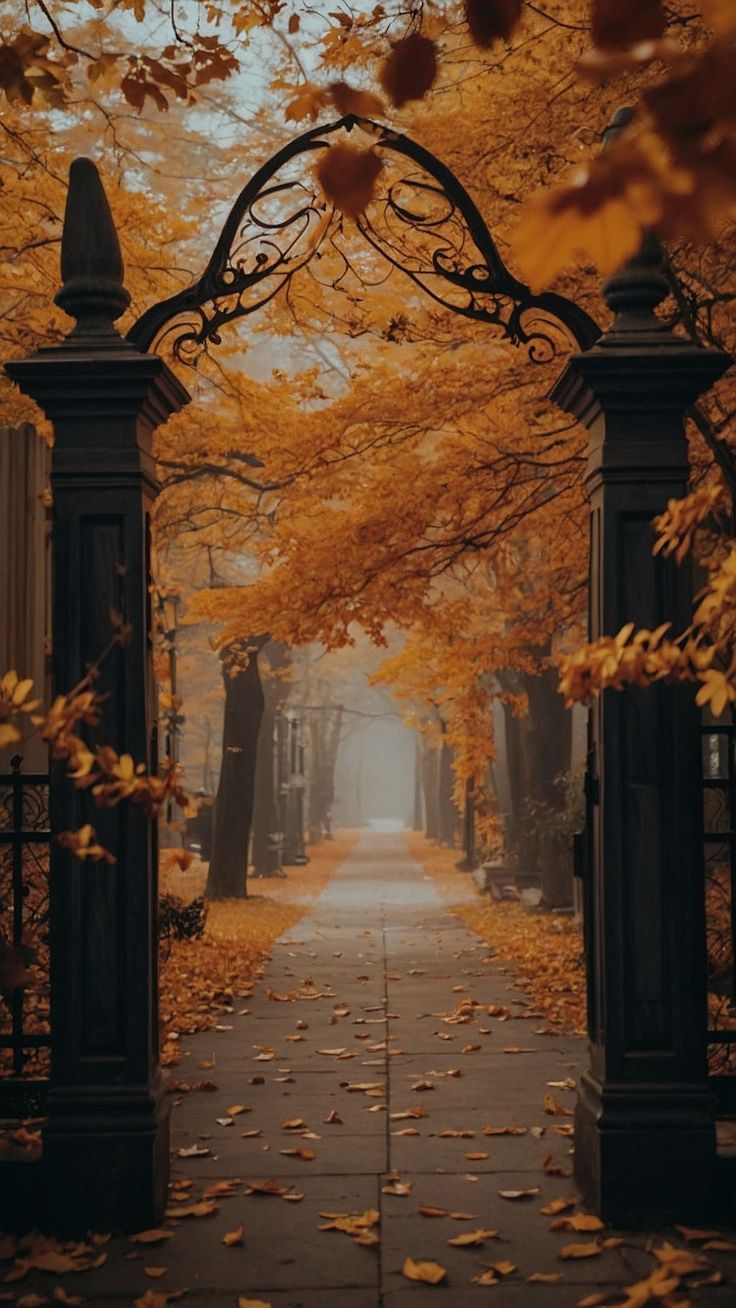 an open gate in the middle of a walkway surrounded by trees with yellow leaves on it