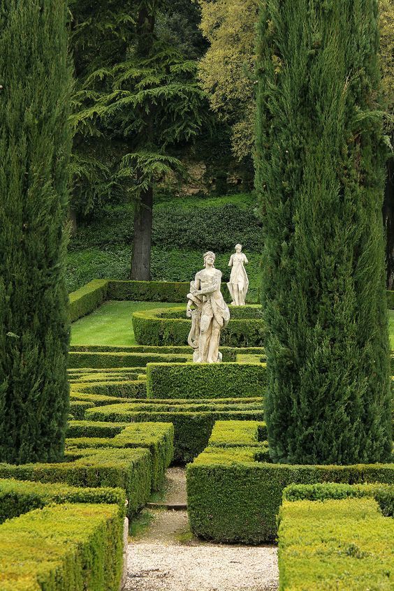 a garden with hedges and statues surrounded by trees