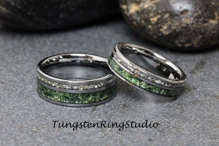 two wedding bands with green and white glitter on them, sitting next to each other