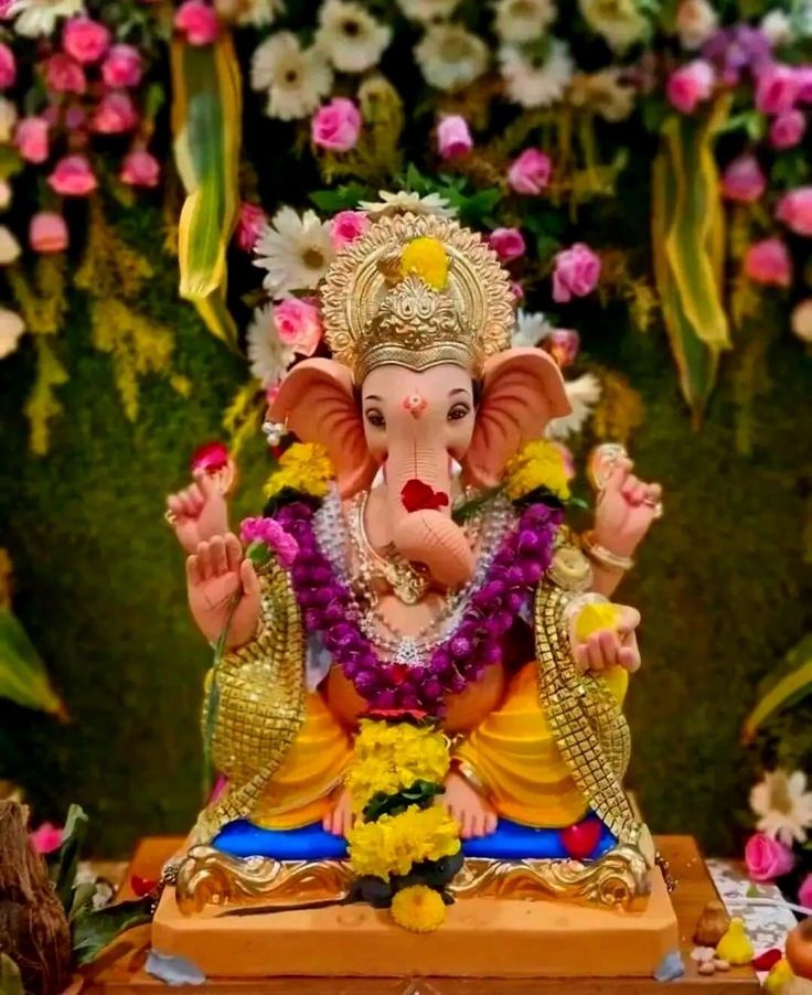 an elephant statue sitting on top of a wooden table next to flowers and greenery