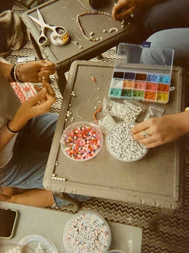 several people sitting at a table with craft supplies on it, including scissors and beads