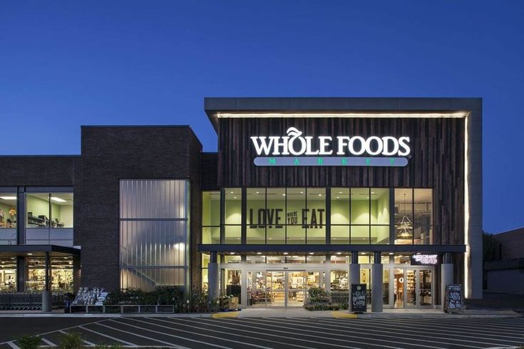 the whole foods store is lit up at night with its logo on it's front