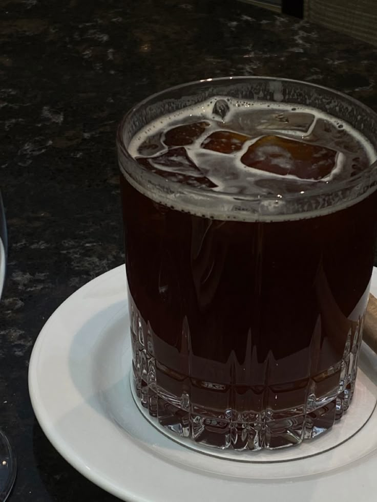 a glass filled with liquid sitting on top of a white plate next to a wooden stick