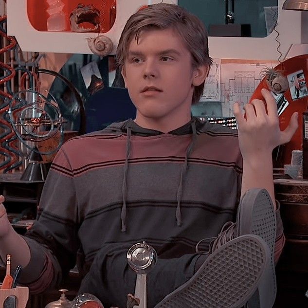 a young man sitting at a desk with his hands in the air