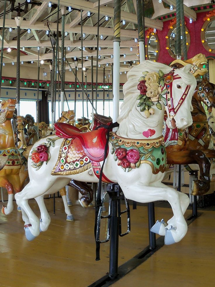 several merry go round horses on display in an indoor area with wooden floors and ceiling lights