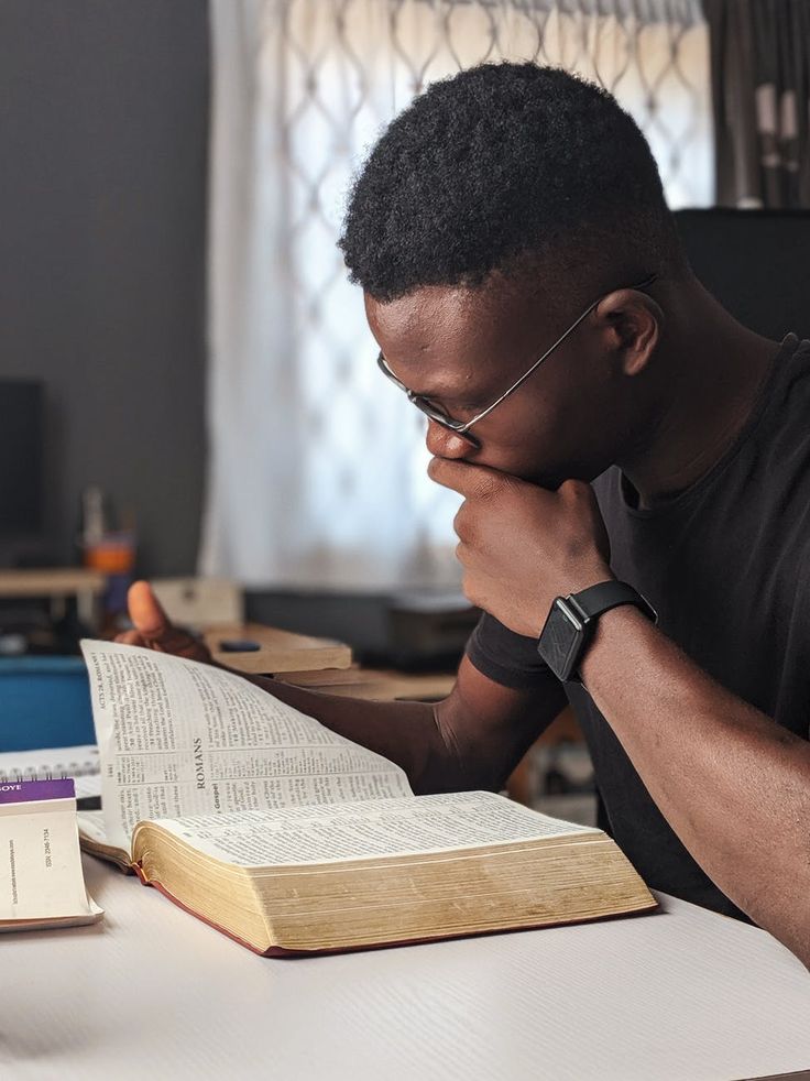 a man sitting at a desk with an open book in front of him, reading the bible