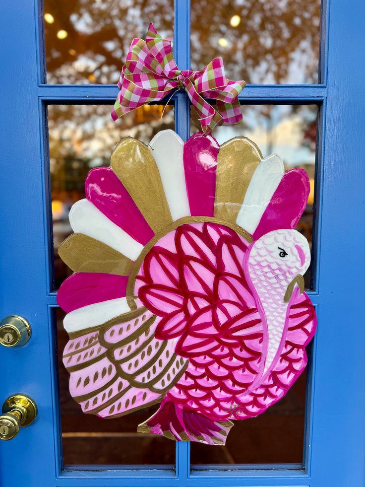 a pink and gold turkey ornament hanging on a blue door with a bow