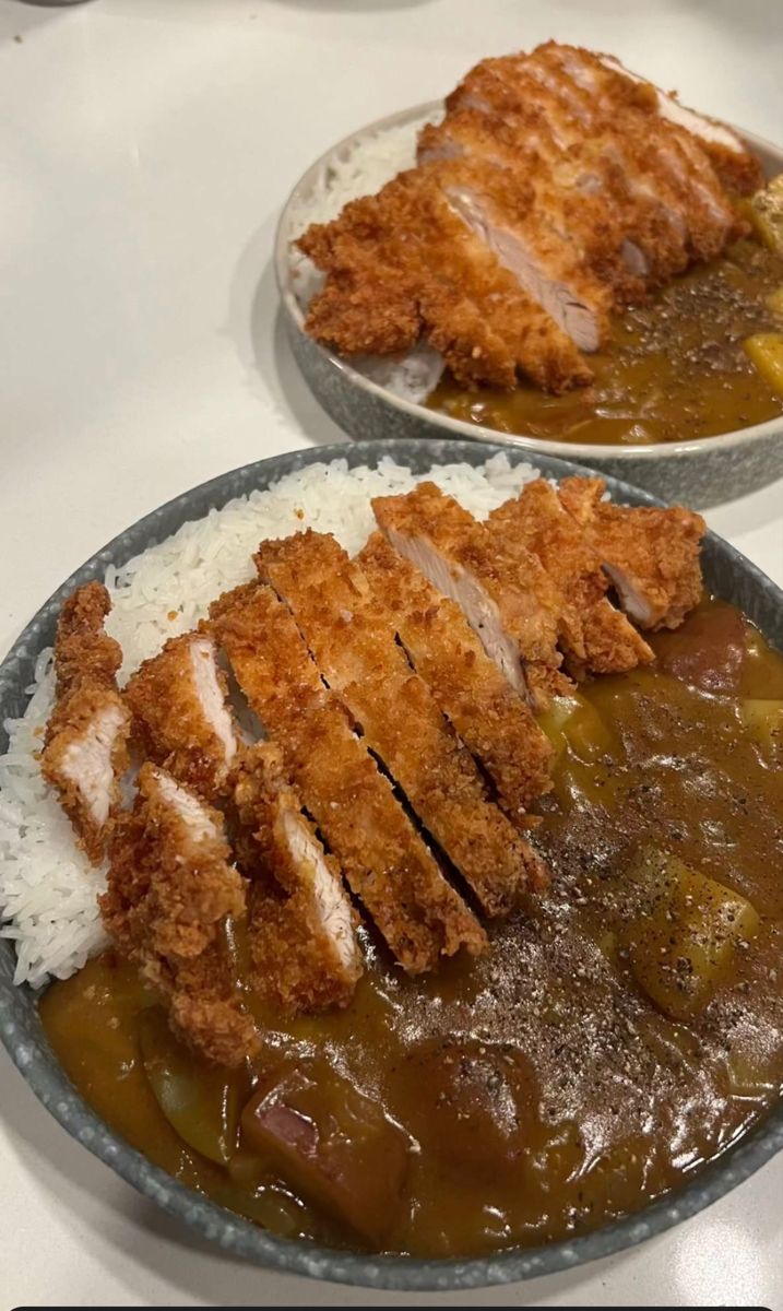 two plates filled with meat and rice covered in gravy