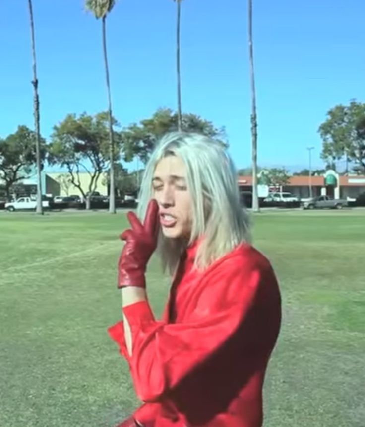 a woman sitting on top of a grass covered field talking on a cell phone with palm trees in the background