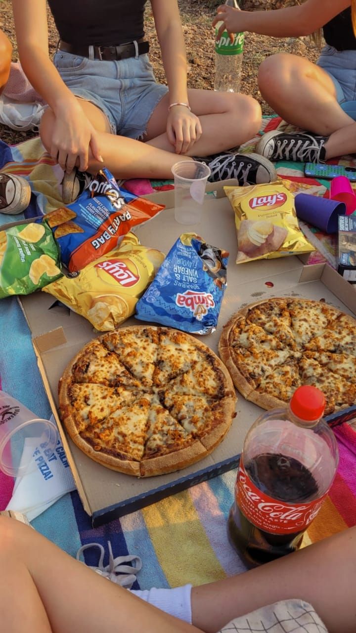 two people sitting on the ground with pizzas and chips in front of them,