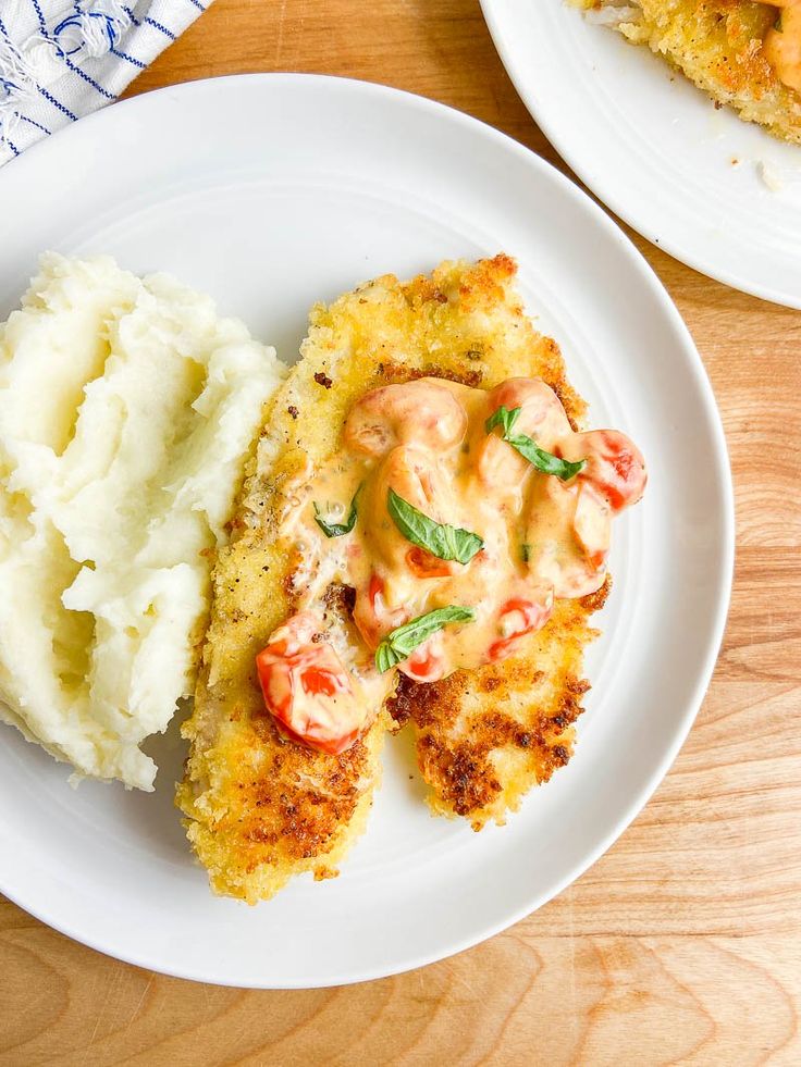 two white plates topped with meat and mashed potatoes on top of a wooden table