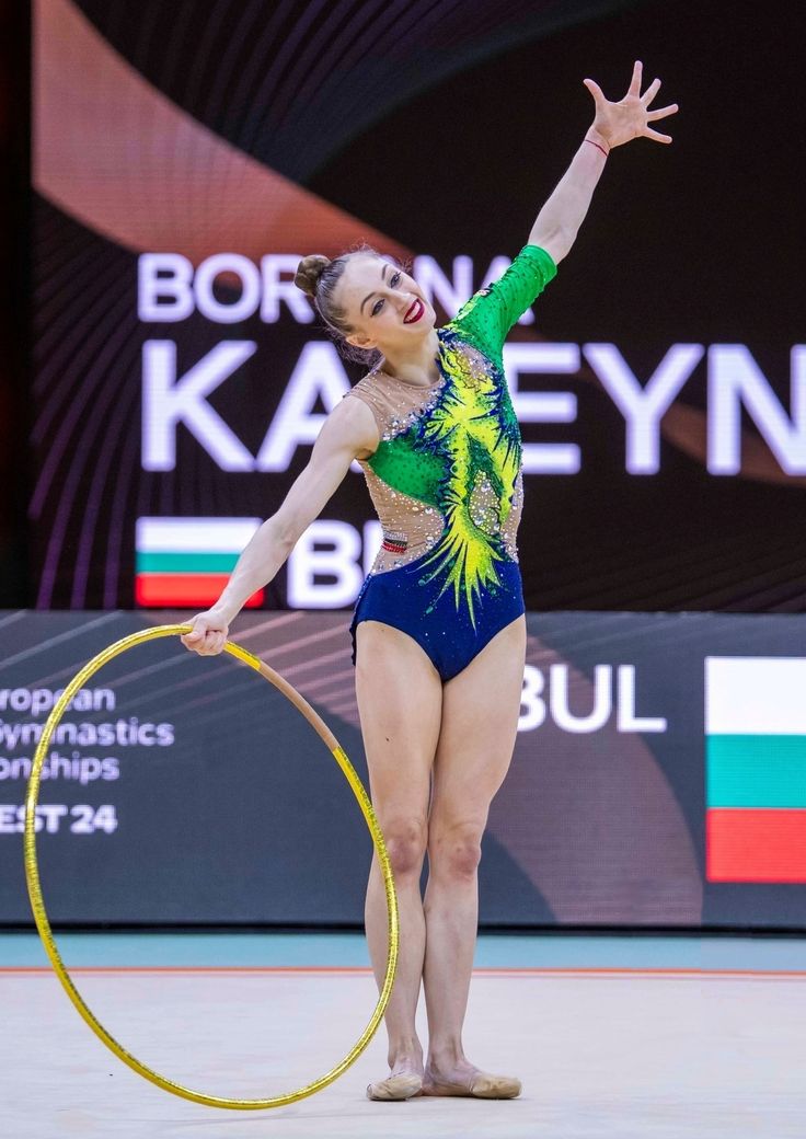 a woman in a green and blue leotard holding a yellow hula hoop