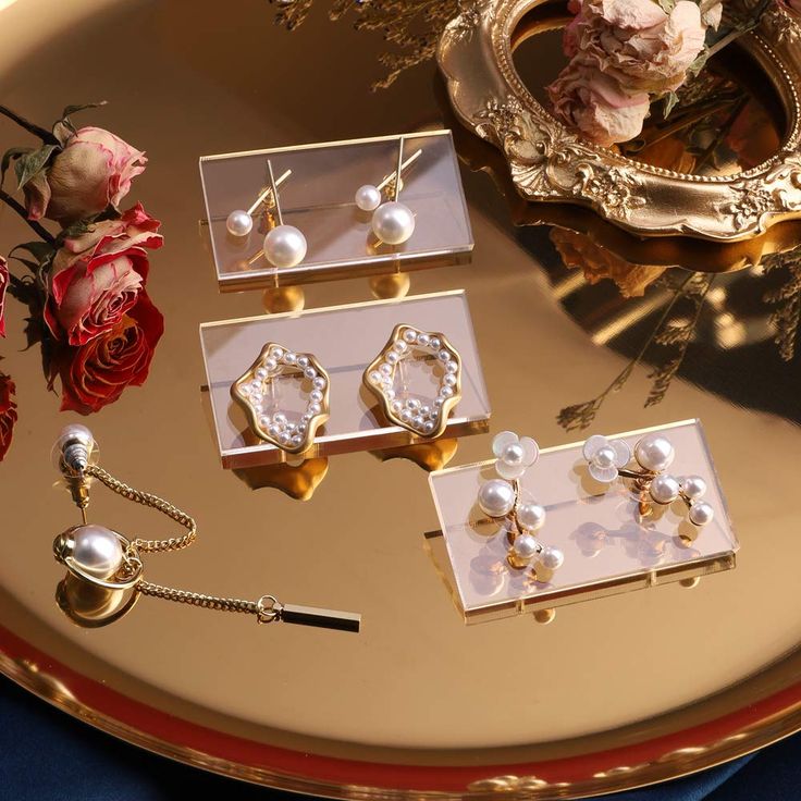 several pairs of earrings on a tray next to flowers and a flower vase with roses in it