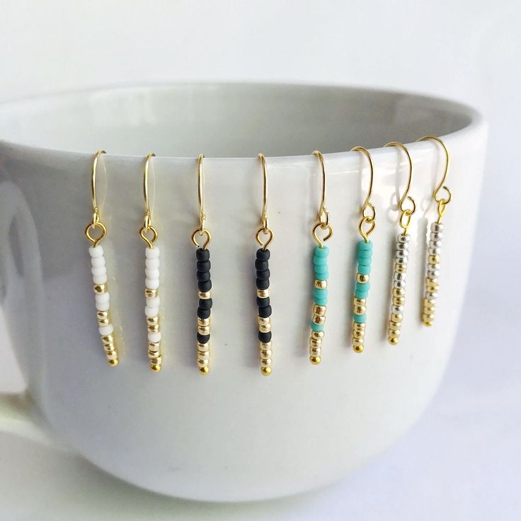 a white cup filled with lots of different colored beads and gold earwires on top of each other