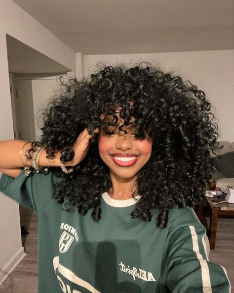 a woman with curly hair is smiling and holding her hands on her head while wearing a green shirt