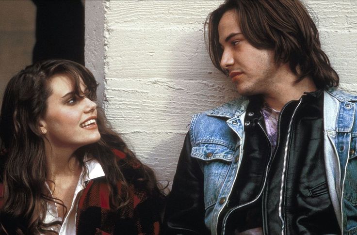 two people standing next to each other in front of a white wall and one person wearing a denim jacket