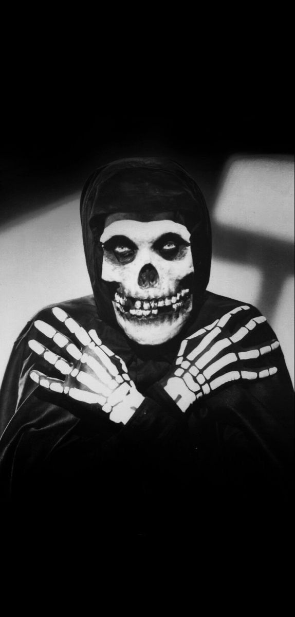 a skeleton dressed in black and white poses for the camera with his hands folded over his chest