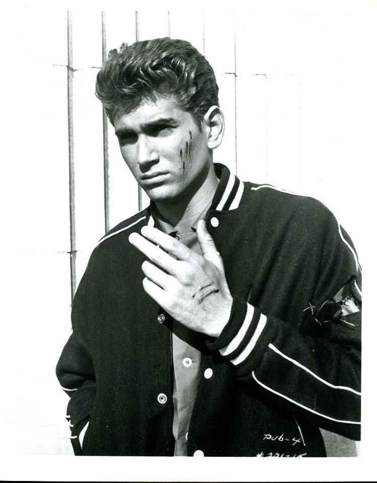 black and white photograph of a young man with his hands on his chest, wearing a baseball jacket