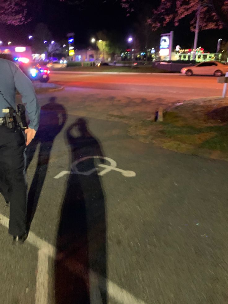 a police officer standing in the middle of an empty parking lot with his shadow on the ground