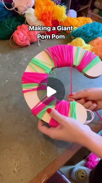 someone making a giant yarn pom pom wreath with colorful yarns on it