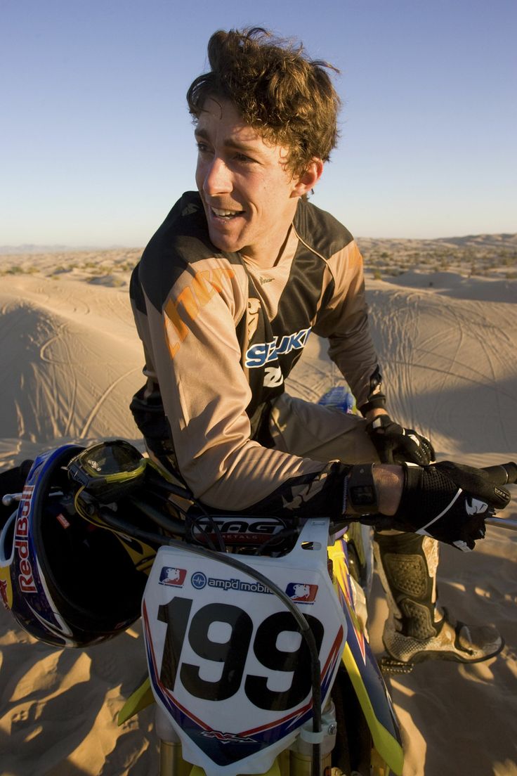 a young man riding on the back of a dirt bike in the sand dune area