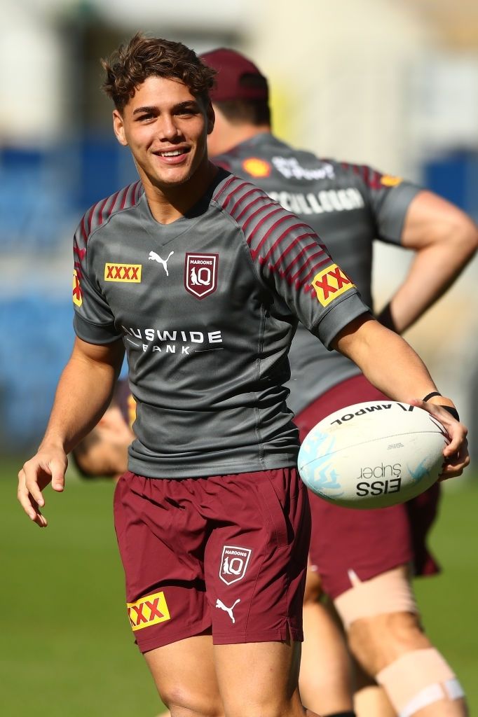 a man holding a rugby ball in his right hand and smiling at the camera with other men behind him