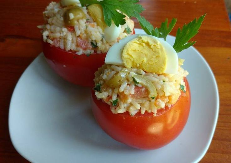 two stuffed tomatoes on a white plate topped with rice and an egg, garnished with parsley