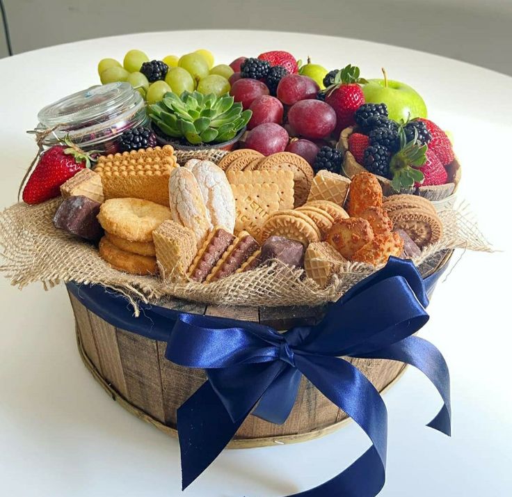 a basket filled with fruit and crackers on top of a white table next to a blue ribbon