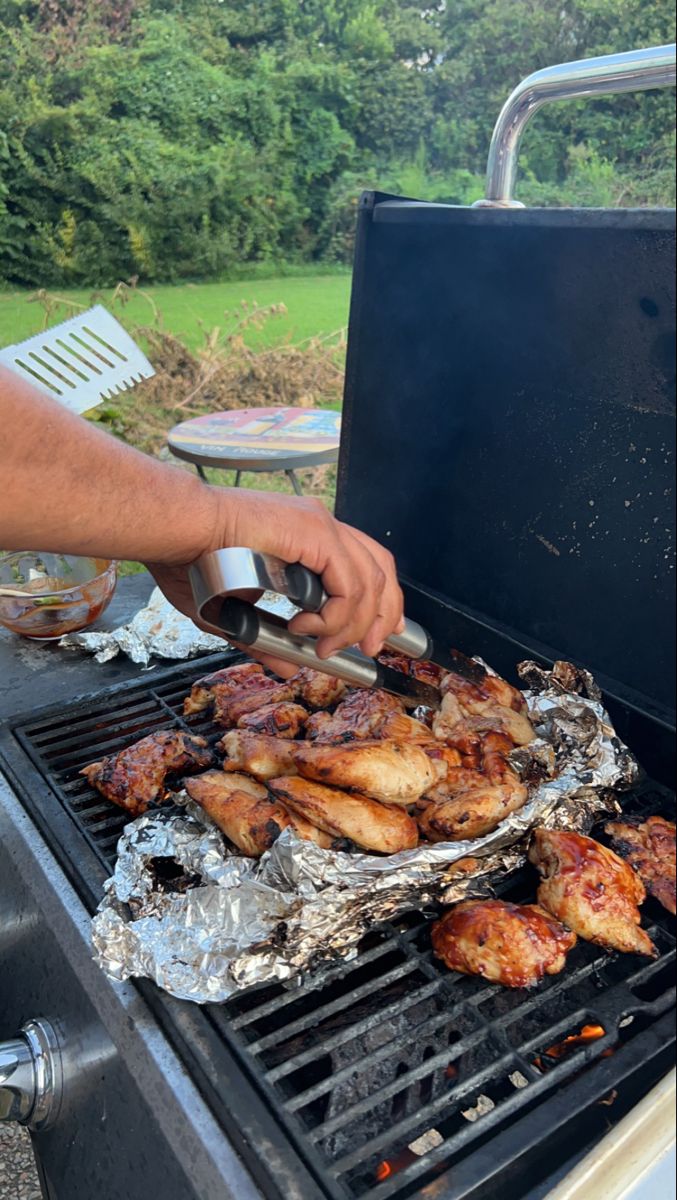 a man grilling chicken on top of a bbq with tongs in his hand