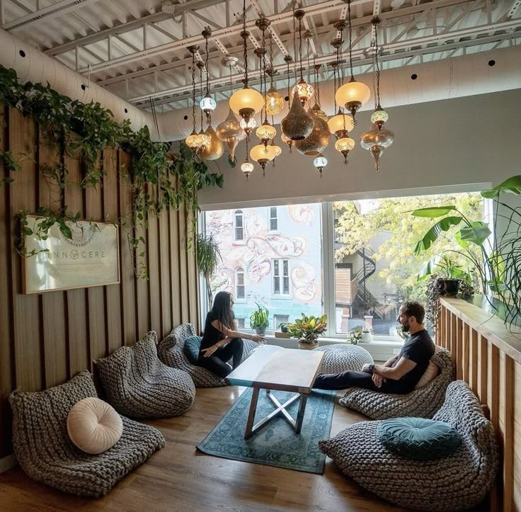 two women sitting on bean bag chairs in front of a window with plants hanging from the ceiling