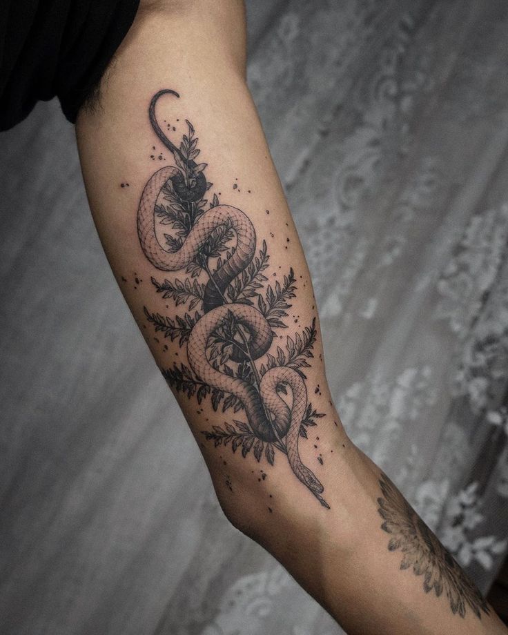 a tattoo on the arm of a man with a snake and flowers around his neck