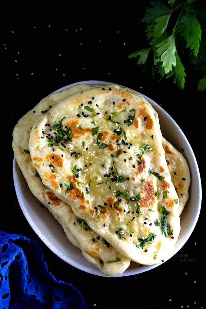 three flat breads on a white plate next to some parsley and blue cloth