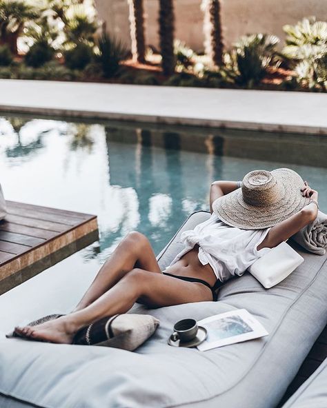 a woman laying on top of a gray couch next to a pool wearing a hat