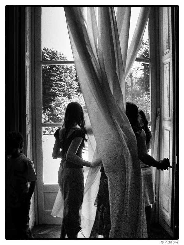 black and white photograph of three women standing in front of a window with drapes