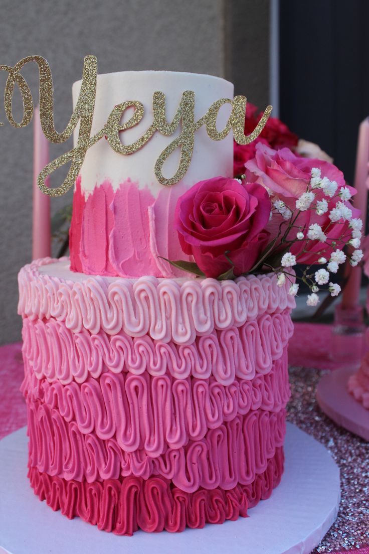 a pink and white cake sitting on top of a table next to candles with flowers