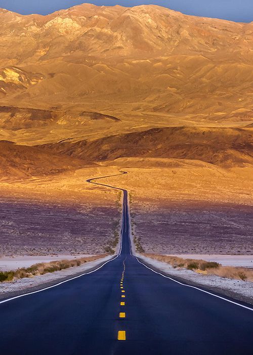 an empty road in the middle of nowhere, with mountains in the backgroud