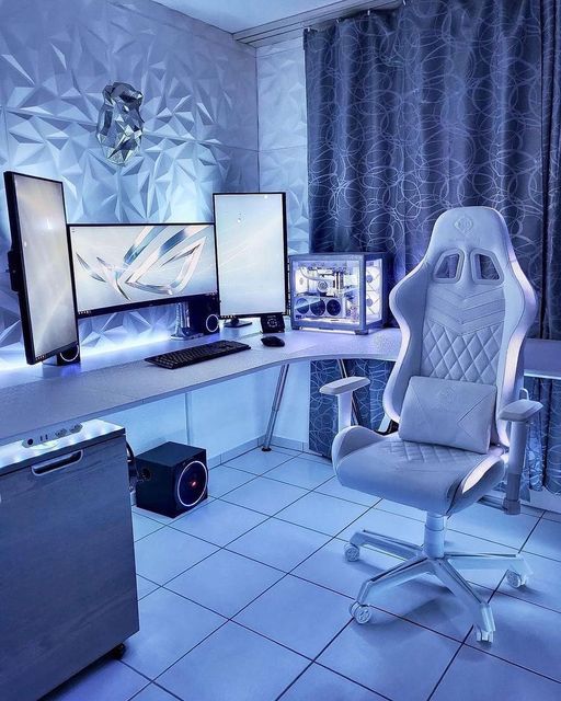 a chair sitting in front of two computer monitors on top of a white desk next to a blue curtain