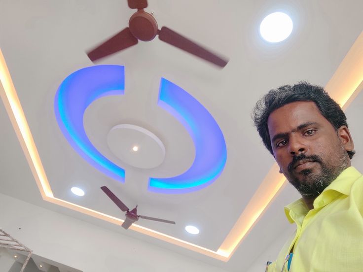 a man standing in front of a ceiling with lights on it and a fan hanging from the ceiling