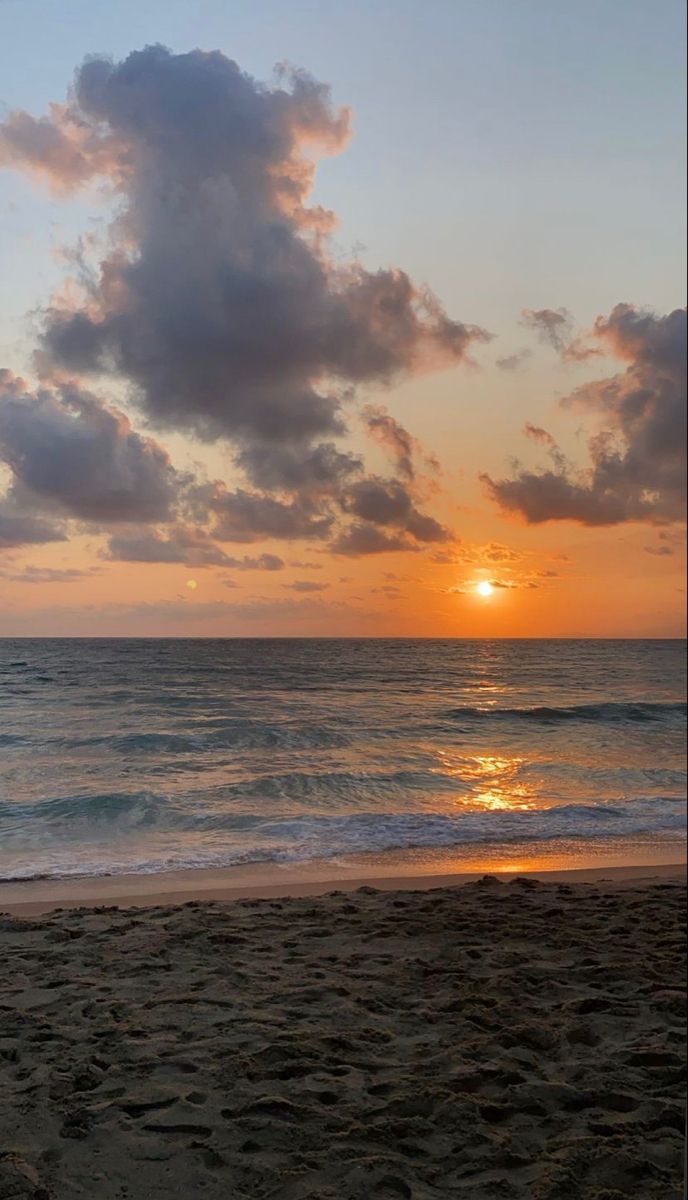 the sun is setting over the ocean with clouds in the sky and on the beach