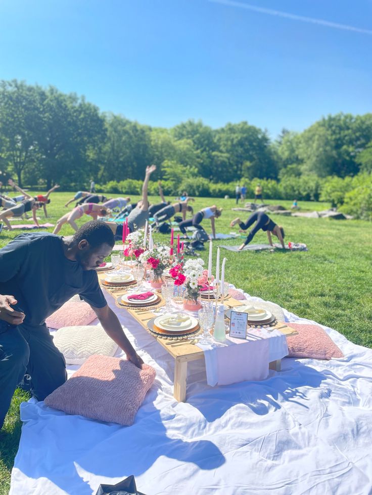 a man is setting up a table in the middle of a field with people doing yoga