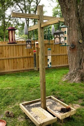 a wooden cross sitting on top of a grass covered field next to a tree and bird feeder