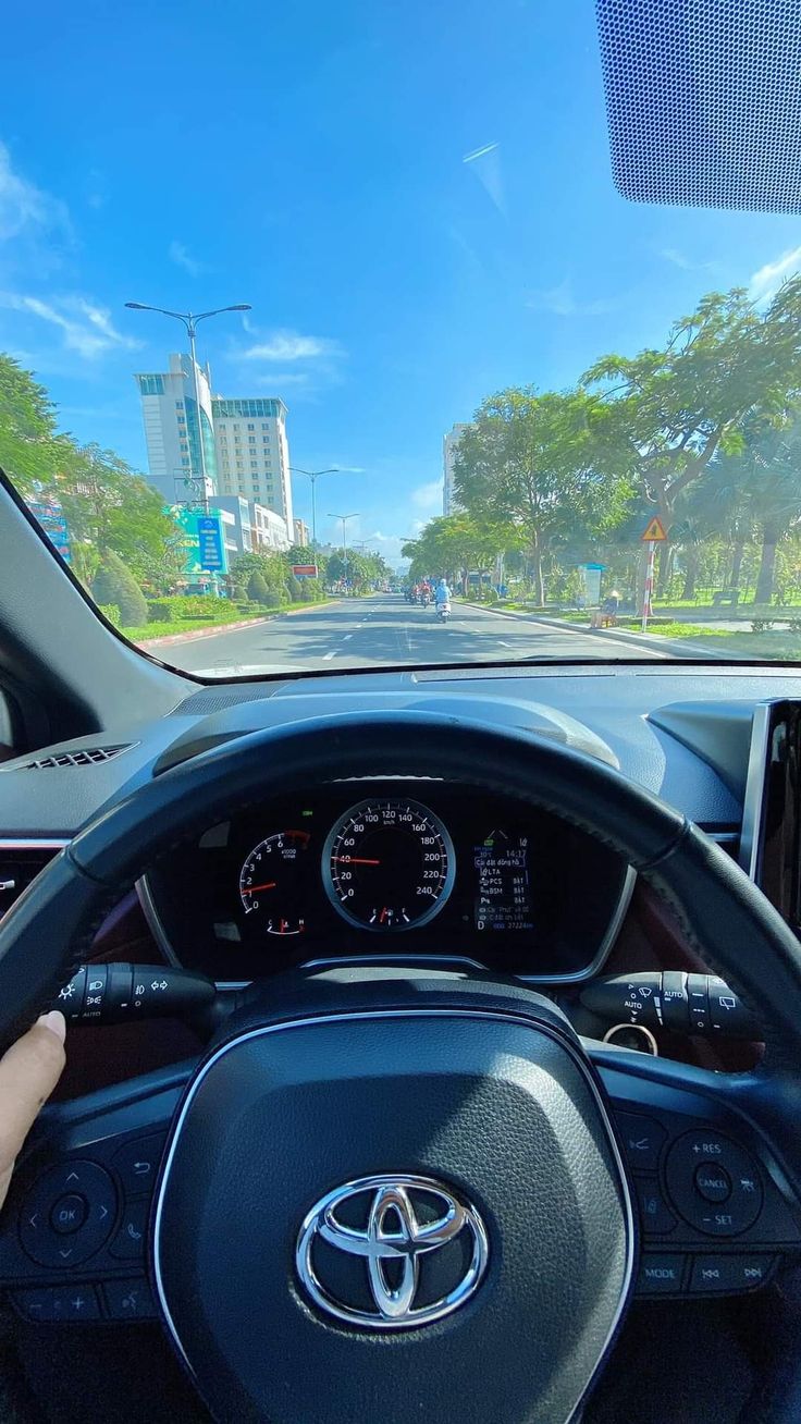 a person driving a car on a road with trees and buildings in the back ground